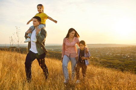 Family in nature at sunset, happiness togetherness. Parents and children walking the golden meadow,...
