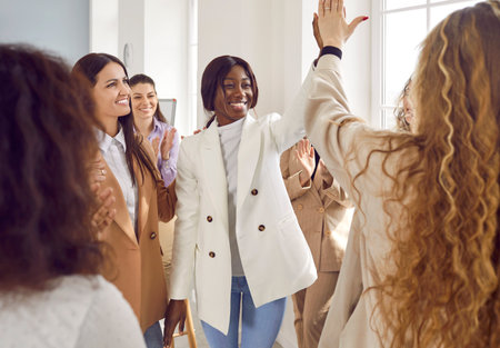 Happy women colleagues giving high five at meeting at the office, celebrating success, making a deal or business achievement. Coworkers applaud congratulating their partners on job well done.の写真素材