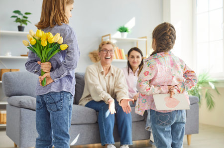 Two children hiding greeting card and tulips behind backs while congratulating grandmother and mother sitting on sofa. Happy family celebrating International Women Day or Mother Day together at home.の写真素材
