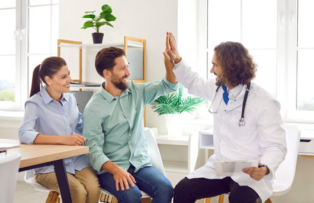 Happy family couple visit doctor together. Cheerful, smiling married man and woman give high five to their doctor. Health care, pregnancy planning, IVF treatment, success conceptの写真素材