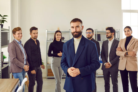Portrait of a young attractive confident boss and business leader proudly looking at the camera with a team of people in background in the office. Business team or group of a staff.の写真素材