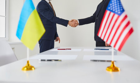 Male politicians from America and Ukraine shake hands after agreeing to sign lend lease for Ukraine. Flags of countries in blurred foreground against background of handshake of diplomats.Cropped imageの写真素材