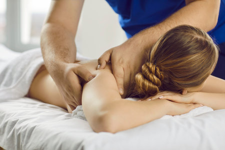 Close up of masseur doing massage to female client in spa or wellness studio. Male therapist works with patient or customer to relieve pain in muscles, help with back pain. Rehabilitation concept.の写真素材