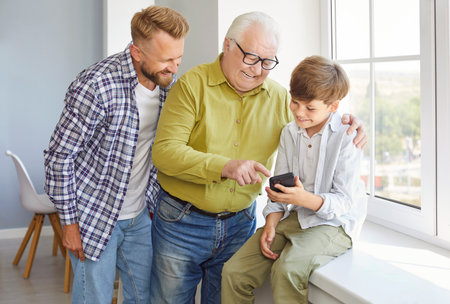 Father, son, and grandfather spend leisure time together at home using a phone for online...