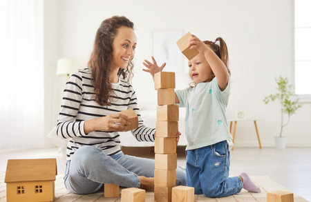 Happy playful smiling mother and baby daughter, babysitter nanny cube block building game, friendly loving family at home close enjoy good time together, parent with cute little girl enjoy weekendの写真素材