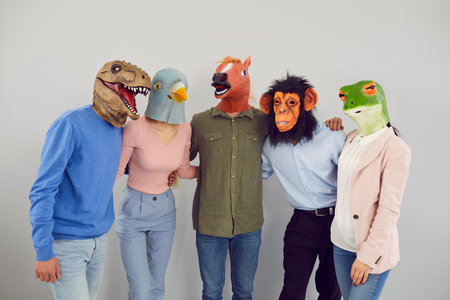 Team of strange people disguised as funny animals. Studio portrait of young men and women wearing crazy eccentric dinosaur, bird, horse, ape and frog masks standing together and hugging each otherの写真素材