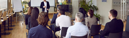 Audience at conference hall. Rear view of people on business training listening to male coach who lectures and trains staff. Business and entrepreneurship concept. Banner. Panorama.の写真素材