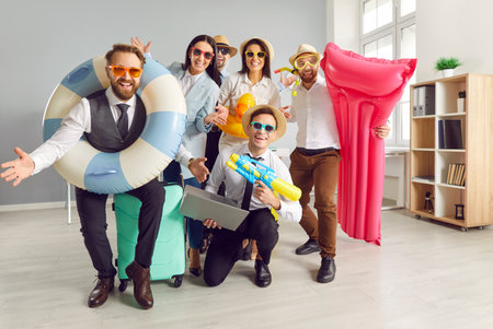 Corporate countdown to summer. Portrait of office workers in high spirits who are enthusiastically preparing for summer vacation. Colleagues hold colorful swimming ring, beach mattress and water gun.の写真素材