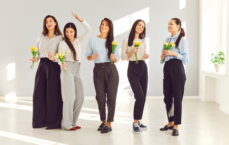 Team of young women with flowers having fun in business workplace on International Womens Day. Group of happy beautiful ladies receive spring tulips at work in office. Holiday, celebration conceptの写真素材