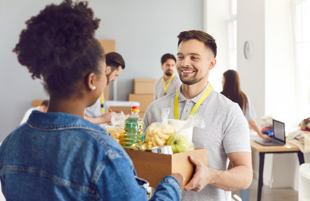 Volunteer man giving box to african american woman, donation to needy, charity, separating donations stuff, basic need provisions, free meal for people in need, food bankの写真素材