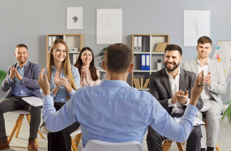 Group of cheerful business people sitting in office and applauding to male speaker during corporate...