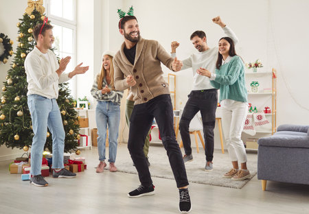 Happy smiling young friends men and women having party and dancing in the living room at home celebrating New Year together. People having fun on Christmas eve enjoying winter holidays.の写真素材