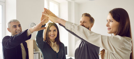 Group of four happy colleagues who raise and join hands to demonstrate unity and solidarity. Men and...