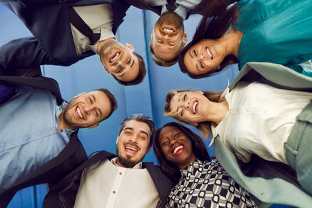 Bottom view portrait of a joyful smiling business people looking down into camera. Happy company employees men and women standing in a circle in office and smiling. Teamwork concept.の写真素材