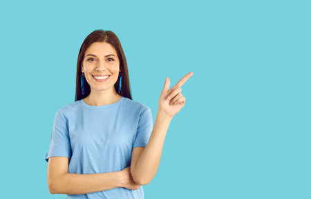 Happy woman standing and showing something on blue copyspace background. Attractive brunette lady in...