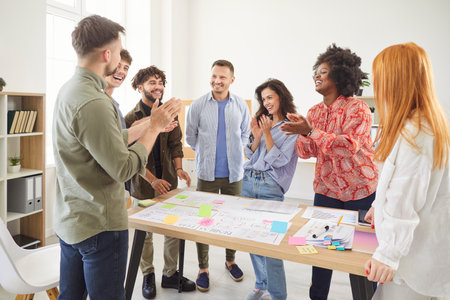 Diverse group of happy young successful business people in casual clothes applauding making a good deal discussing job projects. Coworkers working together at workplace. Teamwork concept.の写真素材