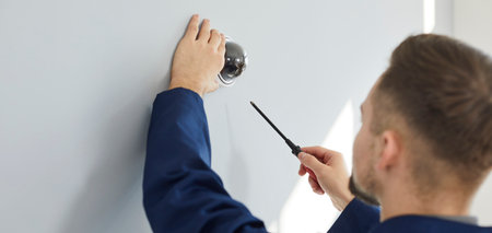 Electrician installing security camera for theft deterrence in building. Repair service worker using screwdriver to fit screws and adjust wall mounted CCTV surveillance dome cam at home or in officeの写真素材