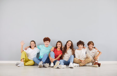 Group of cheerful caucasian high school children in colourful clothes sitting against gray wall and hugging each other. Smiling boys and girls looking at camera and creating joyful memory together.の写真素材