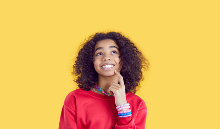 Happy little African American girl teenager looking up with smile and dreaming coming up with idea...