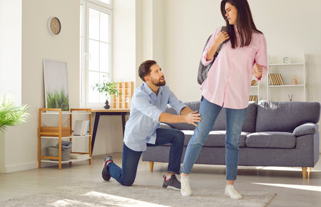 A man at home clings to the leg of a leaving woman, close-up. Concept of a quarrel between a married couple, divorce, end of a relationship. Husband and wife quarreling, negative emotionsの写真素材