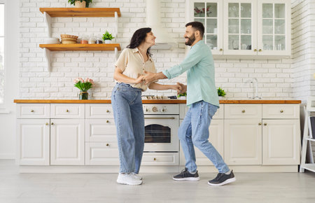 Happy couple dancing together at home, smiling. In a modern kitchen they laugh and sway, sharing happiness, romance, and a trusting relationship. Warm unity, love, lifestyle, and fun concept.の写真素材