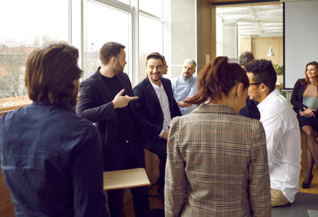 Big group of happy smiling diverse people talking while standing in an office room after a professional business conference, training workshop or corporate work meetingの写真素材