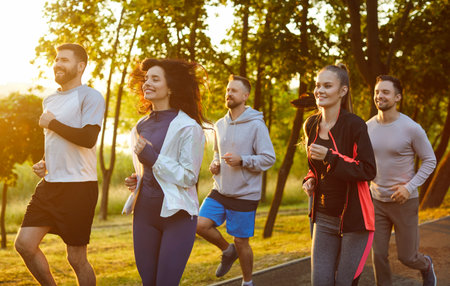 Group of runners jogging together with smiles through summer park in morning outdoor cardio workout....