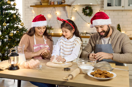 Christmas happy family baking cookies in cozy kitchen. Parents help child girl knead dough, cooking together in festive home. Winter holidays celebration, joy and togetherness concept.の写真素材