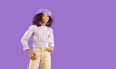 Portrait of cute curly african american preteen little girl isolated on purple background. Beautiful kid girl in elegant casual clothes, in beret and with accessories posing near copy space.の写真素材