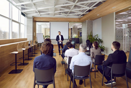 Professional business coach standing by a white board in front of many people in a classroom or...