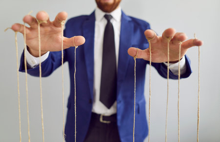 Anonymous adult puppet master, businessman and skillful manipulator makes people obey orders. Midsection. Selective focus close up hands pulling strings tied to fingers. Control, manipulation conceptの写真素材