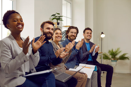 Seminars, trainings and conferences for business people. Group of happy and satisfied people sit in row and applaud their business speaker. Multiracial people with notebooks and laptops in office.の写真素材