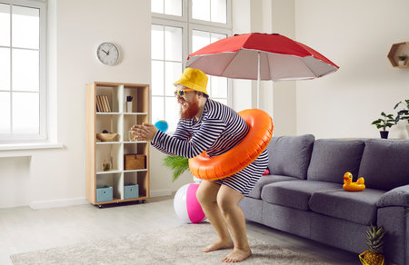 Funny man being at home going on summer vacation and imagining how he dives into sea. Side view of man in striped swimsuit and with inflatable circle at waist imitates diving in living roomの写真素材