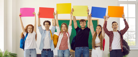 Group of happy positive students holding colourful files above their heads in classroom. They are smiling and looking at camera. concept of education, studying in highschool, college, university.の写真素材
