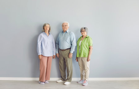 Full length portrait of senior man and women standing together isolated on grey wall background. Group of elderly people in smart casual clothes looking at camera, smiling and making group photo.の写真素材