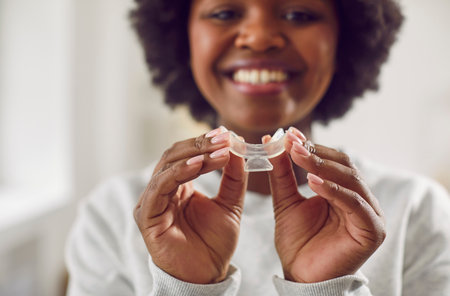 Happy beautiful African American woman holding a teeth whitening tray. Closeup of hands holding a...