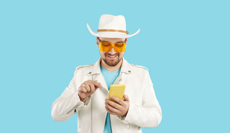 Happy young stylish man in cowboy hat and sunglasses isolated on blue studio background text message...