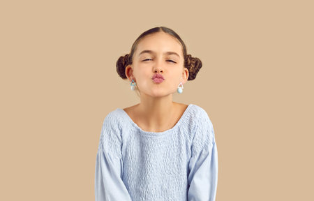 Portrait of lovely funny cute kid girl making air kiss on camera on beige studio background. Beautiful stylish caucasian preteen girl with hairstyle with two bundles makes lips for kiss. Banner.の写真素材