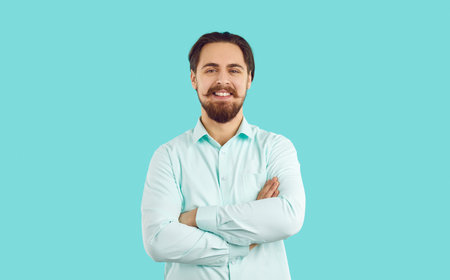 Portrait of smiling young bearded male employee or worker isolated on blue studio background. Headshot of happy confident man in formalwear with arms crossed. Success and employment.の写真素材