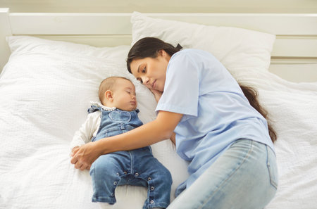 Top view of relaxed young mother lying in bed next to peacefully sleeping toddler child. Caring...