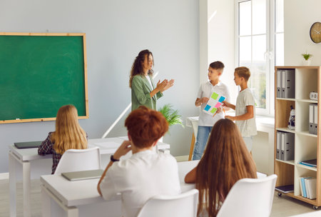 Two students presenting a project or classwork during a lesson with the teacher in a school classroom. This activity highlights studying, learning, and teamwork in educational environment.の写真素材