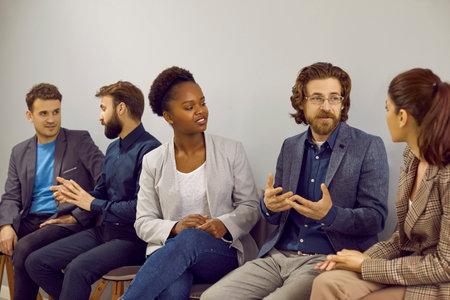 Group of diverse business people sitting in a row and talking. Team of multiracial young men and women attend a business seminar, meet in the office, learn new things and discuss different questionsの写真素材