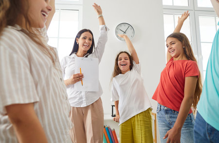 Group of happy school children with their young friendly female teacher or psychologist standing in a circle in the classroom with hands up together. Back to school, education and teamwork concept.の写真素材