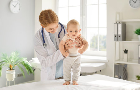 Pediatrician medical doctor exam, checking baby body tension or muscle tone, treats newborn in clinic, monitoring child physical health, development, providing care, diagnosing standing positionの写真素材