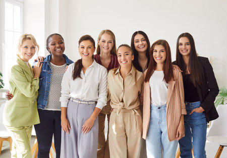 Portrait of happy smiling young diverse female company employees wearing casual clothes in modern office and looking cheerful at camera. Women collogues and coworkers standing in a row indoorsの写真素材