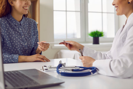 Woman comes to the clinic or hospital and gets a prescription from her doctor. Smiling specialist gives a prescription to a happy young woman. Medicine and health conceptの写真素材