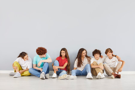 Happy group of children sits together on the floor, posing for a team portrait against a grey background. The students, pupils are part of a diverse and joyful community, showcasing togetherness.の写真素材