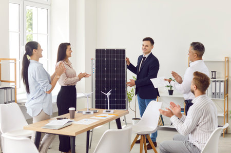 Smiling confident project manager presents renewable energy sources solar panel in a business people meeting for team in an office. Company employees applauding to colleague after presentation.の写真素材