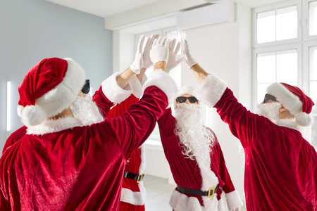 Group of Santas friends wearing sunglasses raising hands high-fiving, celebrating together, cheerful fun, representing teamwork and festive spirit, festive holiday performance gathering meetingの写真素材