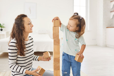 Happy daughter plays with wooden toys with her mother, spending restful, joyful moments together at home. Family leisure time is filled with smiles, fostering warmth and connection.の写真素材